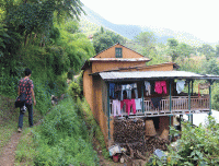 Man walking down hillside next to house on Chamapadevi Day Hiking trail in village, showcasing local lifestyle and old houses.